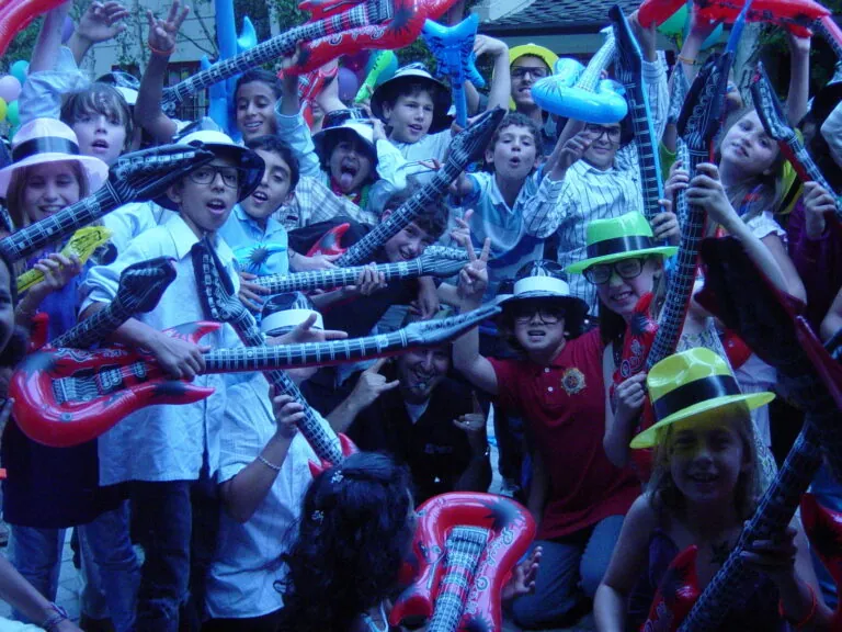 Kids in party hats waving inflatable guitars at a fall festival.