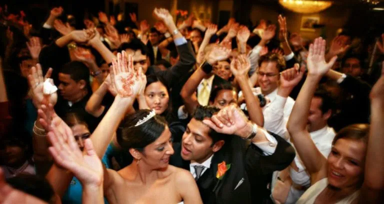 Wedding guests cheering with their hands raised under warm light.