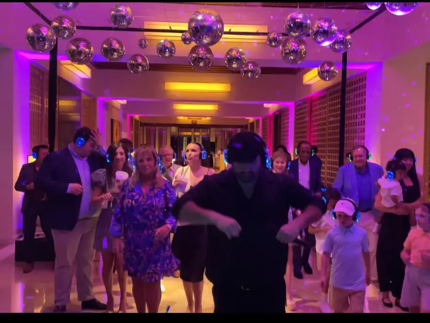 Guests dance under mirror balls and pink uplights at a company party.