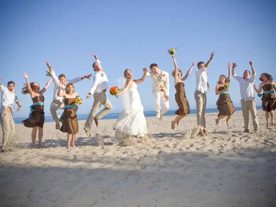 A wedding party jumping for joy on the beach.
