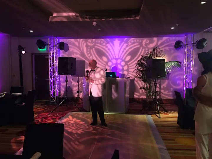 A DJ setup in a room washed in purple uplights with a gobo pattern on the wall.