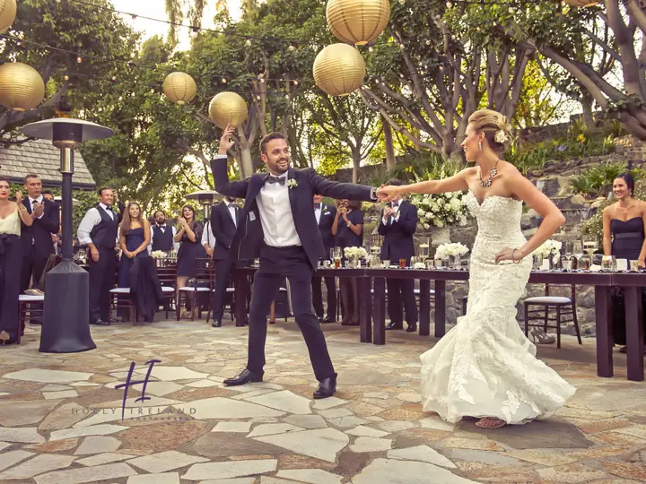 A bride and groom dancing on an outdoor patio while guests watch.