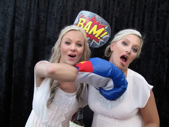 Two guests hamming it up with a boxing glove and a BAM! sign in the photo booth.