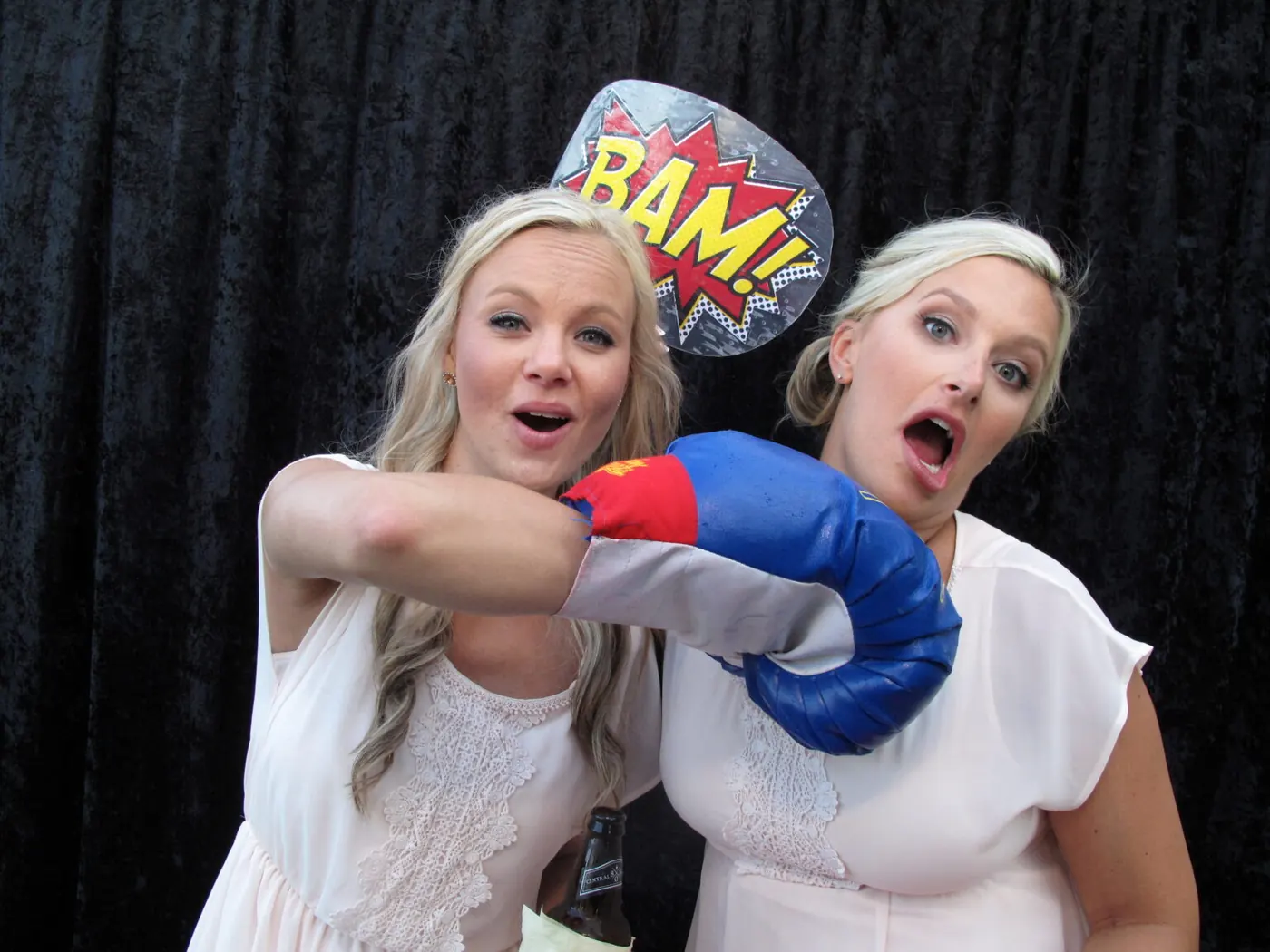 Two guests hamming it up with a boxing glove and a BAM! sign in the photo booth.