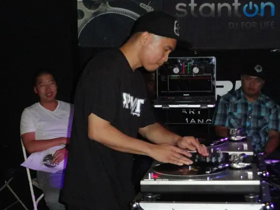 Francis scratching on two turntables while friends watch.