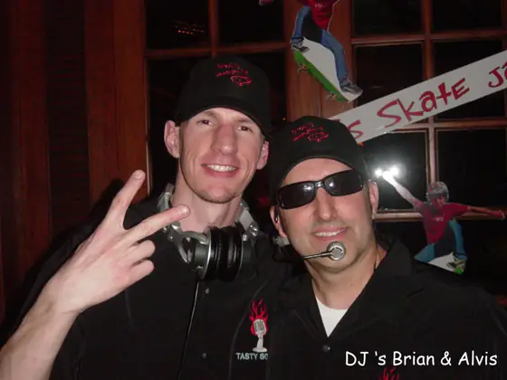 DJs Brian and Alvis, headphones on, smiling for the camera at a party.