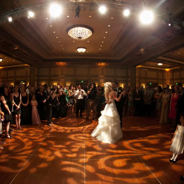 A bride dancing on an amber gobo-lit ballroom floor while guests watch.