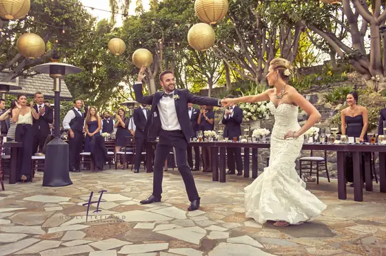 A bride and groom dance on an outdoor stone patio under strings of round lanterns.