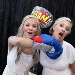 Two guests hamming it up with boxing gloves and a BAM! sign in a photo booth.