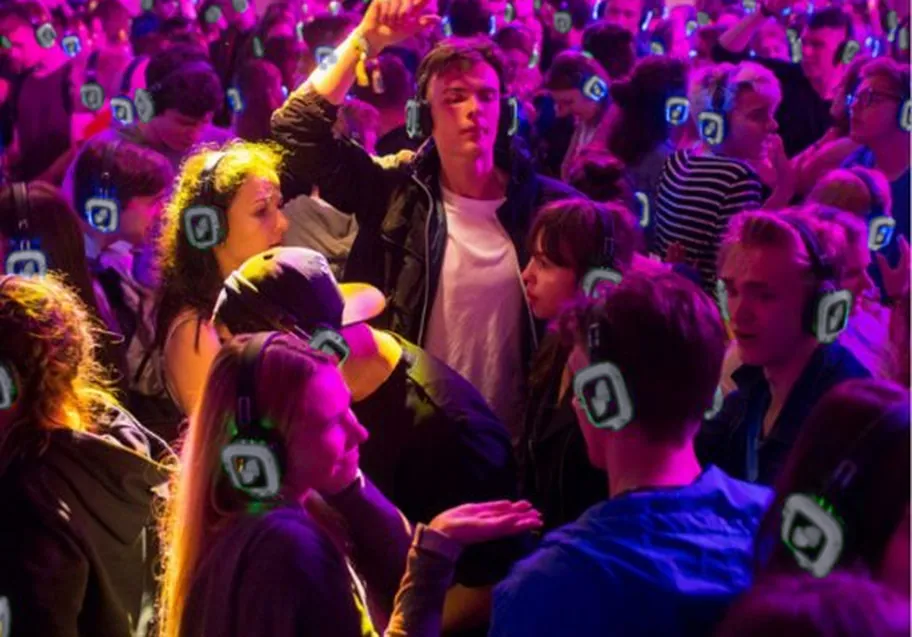 A packed dance floor of guests wearing light-up wireless headphones, each headset glowing the colour of the channel it is tuned to.