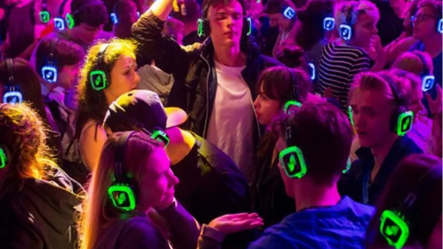Guests in glowing green and blue headphones on a crowded dance floor.